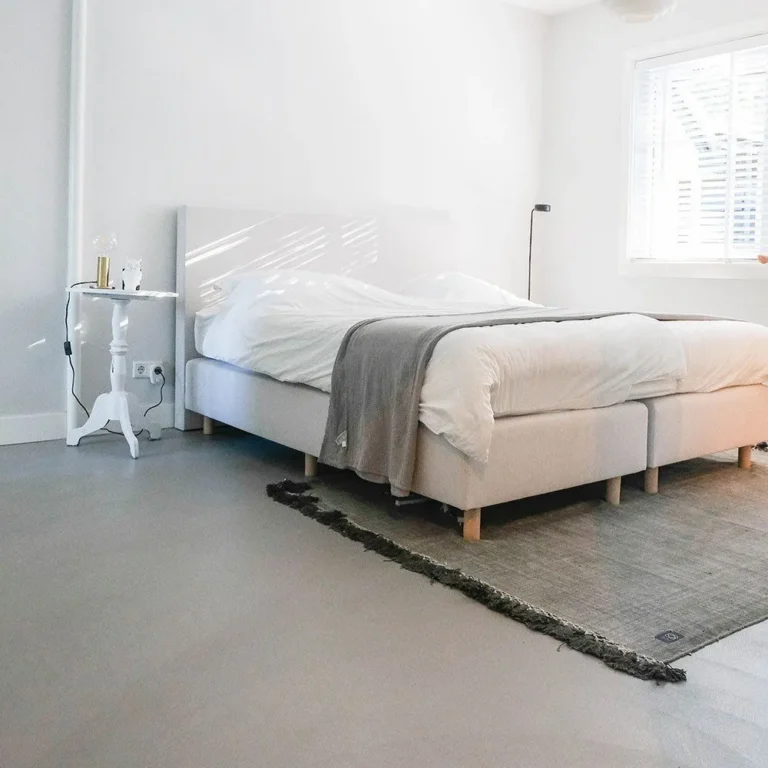 Schlafzimmer mit fugenlosem grauem Boden und hellem Bett