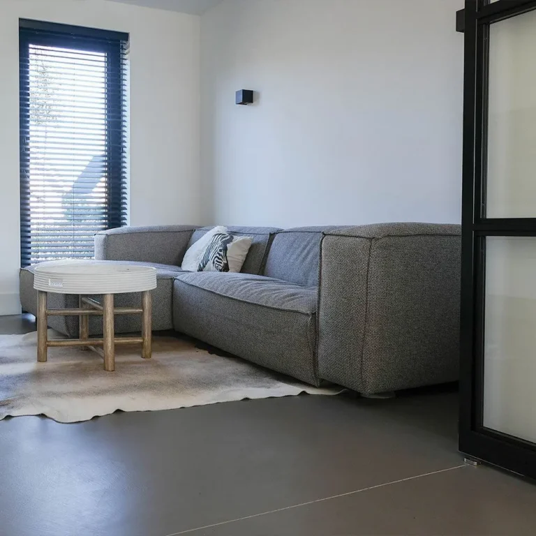 Wohnbereich mit dunklem fugenlosem Gießboden, grauem Sofa und großem Fenster